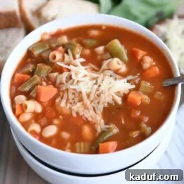 Minestrone soup in two stacked white bowls with parmesan cheese