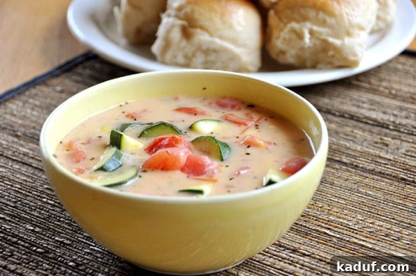 Summer's Bounty Vegetable Soup 2 A steaming bowl of Summer Garden Vegetable Soup, rich with chunks of zucchini and vibrant red tomatoes, served with a side of freshly baked rolls.