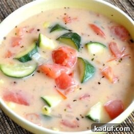 A bowl of creamy summer vegetable soup garnished with fresh herbs.