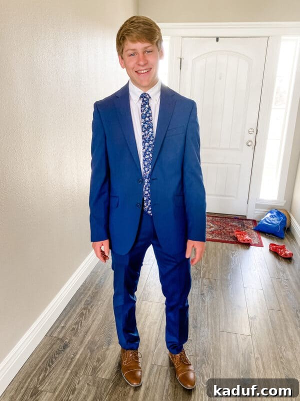 Friday Reflections: Life Lately and Finding My Rhythm 3 A teenager in a sharp blue suit stands confidently next to a wall, ready for his first prom, a poignant blend of joy and underlying sorrow.