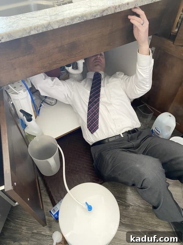 Friday Reflections: Life Lately and Finding My Rhythm 7 A man, still in a shirt and tie, diligently fixes something underneath a sink, illustrating the relentless nature of daily chores.