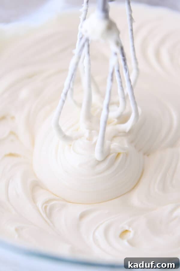 Zesty Lemon White Chocolate Squares 4 Whipping creamy cheesecake batter in a clear glass bowl with an electric hand mixer.
