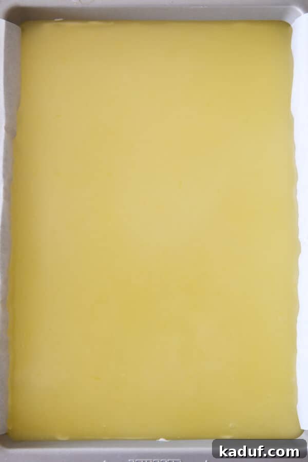 Zesty Lemon White Chocolate Squares 7 Lemon topping being spread on top of the cheesecake layer for lemon white chocolate cream bars.