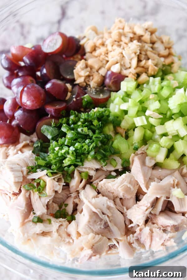 Shredded chicken, green onions, celery, grapes and nuts in glass bowl.