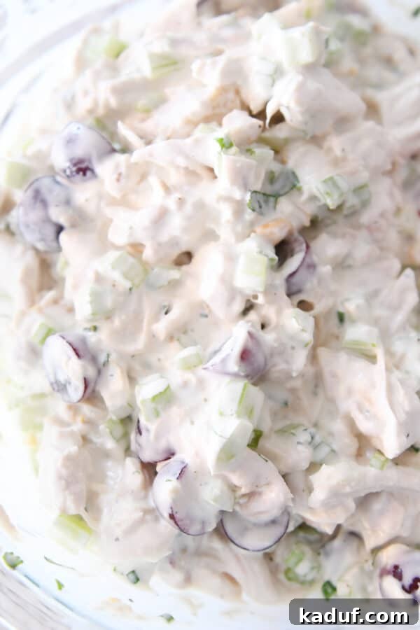 Chicken salad ingredients with creamy dressing in glass bowl.