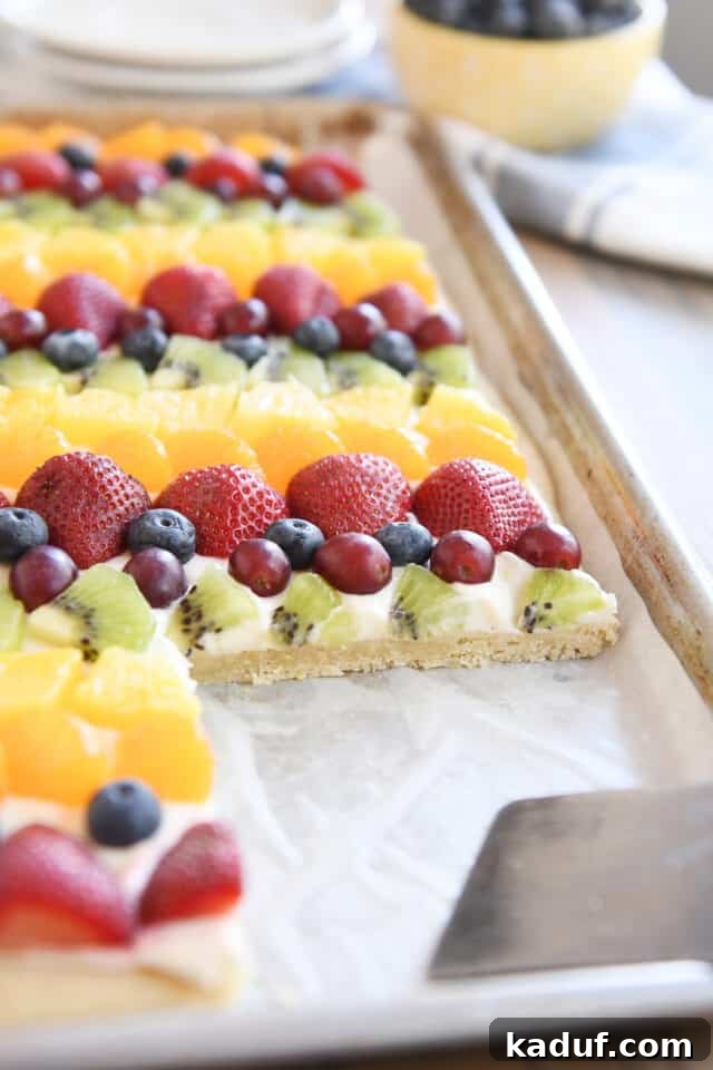 The Perfected Fruit Pizza 9 Sheet pan of fruit pizza with a serving taken out with metal spatula.
