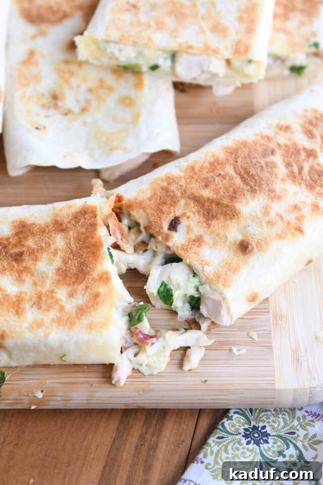 Ultimate Crispy Chicken Bacon Ranch Wraps 7 Two halves pulling apart of crispy chicken bacon ranch wrap on wood cutting board.
