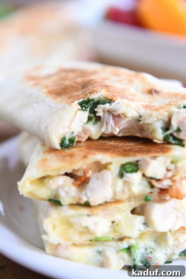 Ultimate Crispy Chicken Bacon Ranch Wraps 8 Bite taken out of crispy chicken bacon ranch wrap stacked on other wraps on white plate.