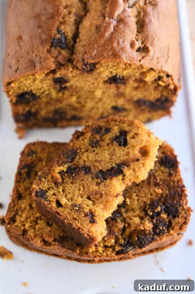 Spiced Pumpkin Chocolate Chip Loaf 6 A half slice of moist pumpkin chocolate chip bread artfully placed on top of two full slices on a pristine white platter, highlighting its beautiful texture and visible chocolate chips.