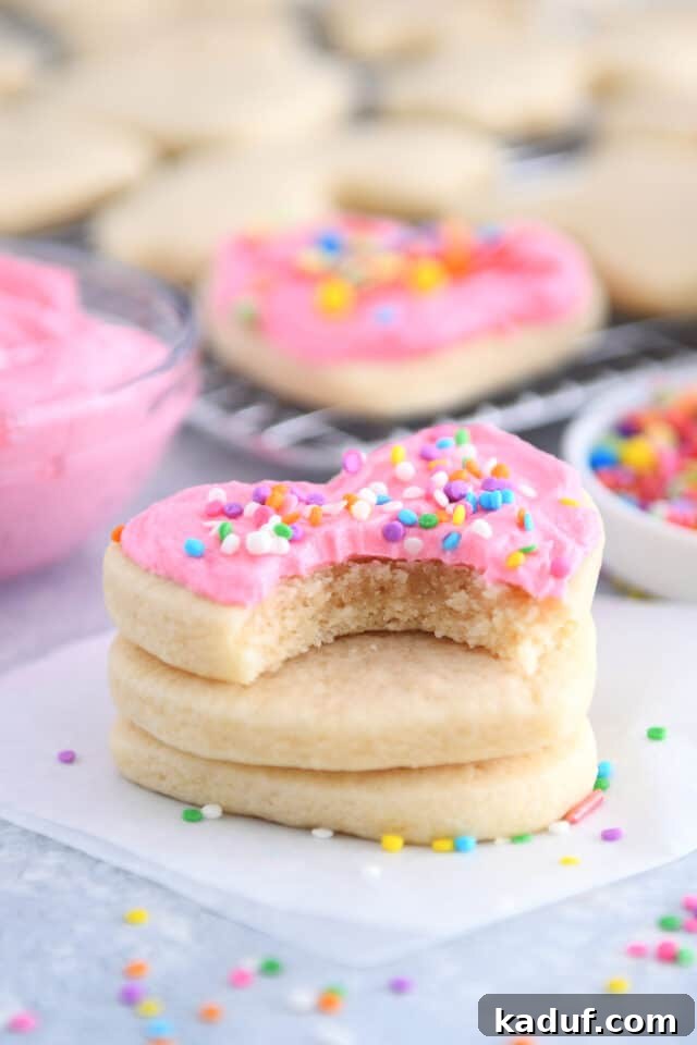 The Ultimate Cutout Sugar Cookie Recipe 11 Bite taken out of pink frosted heart shaped sugar cookie stacked on two unfrosted cookies.
