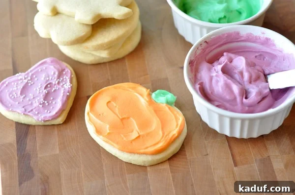 The Ultimate Cutout Sugar Cookie Recipe 14 Frosted heart and pumpkin sugar cookies, with ramekins of pink and green frosting and a stack of unfrosted sugar cookies all on a brown table.