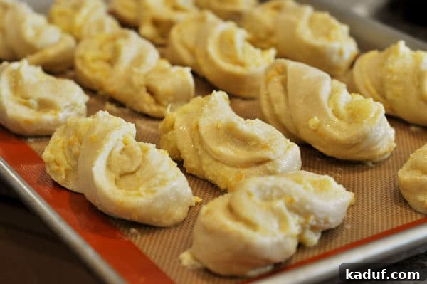 Orange Glazed Sweet Rolls 11 uncooked twisted orange rolls lined up on a sheet pan