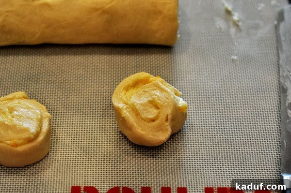 Orange Glazed Sweet Rolls 8 Uncooked filled orange rolls on a sheet pan.