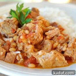 A bowl filled with tender pork, white beans, and kielbasa in a rich, flavorful broth, ready to be served.