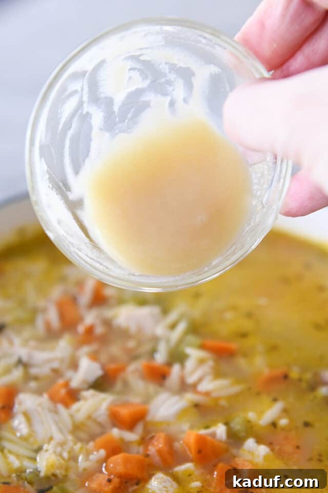Bright Lemon Chicken Orzo Soup 6 A chef's hand adding a mixture of melted butter and flour (roux) to a pot of lemon chicken orzo soup, illustrating the optional thickening step.