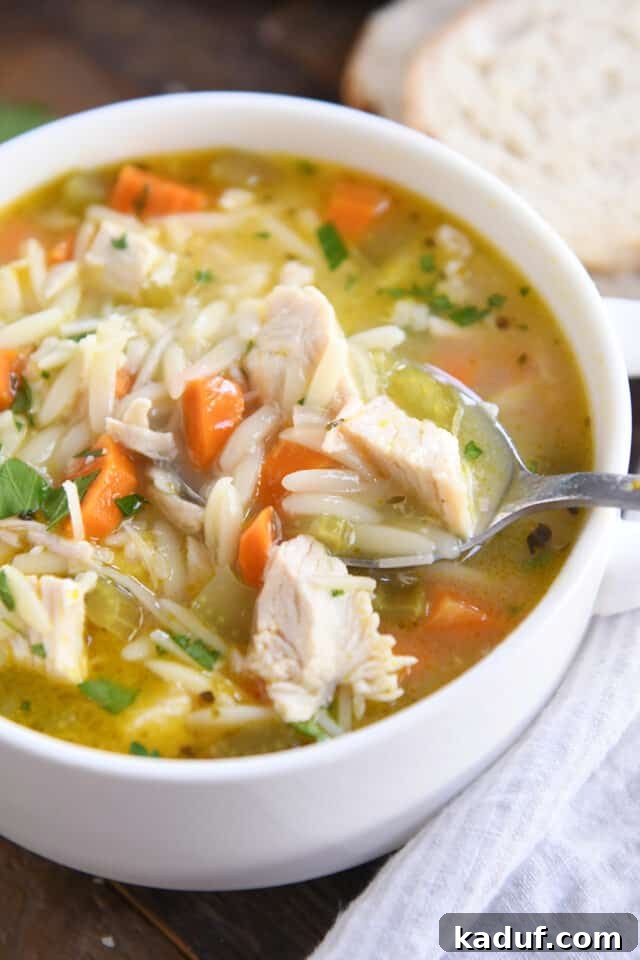 Bright Lemon Chicken Orzo Soup 7 A spoon delicately scooping a generous portion of lemon chicken orzo soup from a white bowl, showcasing the tender chicken, orzo, and vibrant broth.