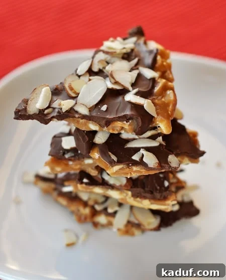Golden Almond Toffee 2 Pieces of almond roca stacked on a white plate, showcasing its golden toffee, chocolate, and almond layers.