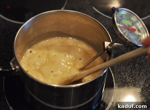 Golden Almond Toffee 12 Saucepan full of bubbling butter mixture with a wooden spoon and candy thermometer clipped to the side, showing continuous cooking.