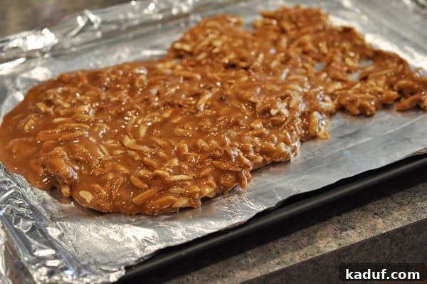 Golden Almond Toffee 15 Caramel and almonds mixture being spread on a tinfoil lined cookie sheet, a quick step before it hardens.