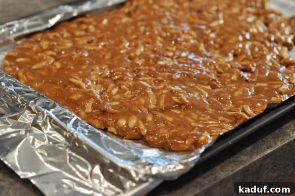 Golden Almond Toffee 16 Caramel coated almonds spread out on a tinfoil lined sheet pan, showing the thin layer of toffee.