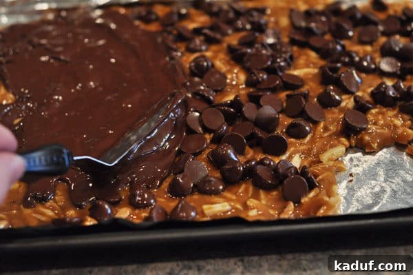Golden Almond Toffee 20 Offset spatula spreading melted chocolate over chocolate chip covered almond roca, creating a smooth, glossy top.