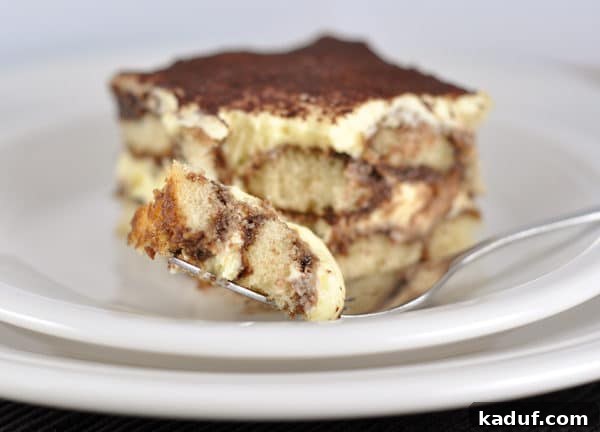 Decadent Chocolate Tiramisu 3 A close-up of a tiramisu slice on a white plate, with a small bite taken out, revealing the soft interior layers.