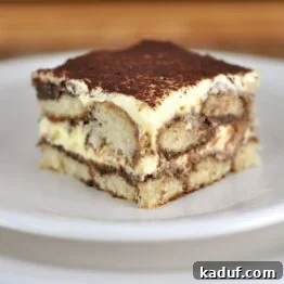 Close-up of a chocolate tiramisu slice on a white plate with a fork.