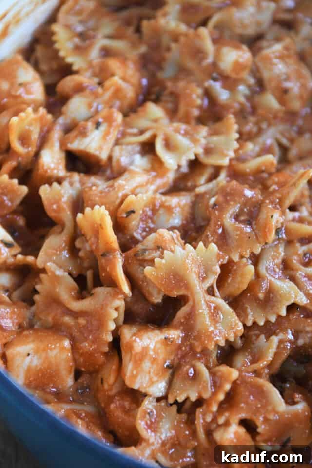 Effortless One-Pot Chicken Lasagna 6 Cooked bowtie pasta and chicken in a rich tomato sauce in a blue pot, showcasing the finished dish before serving.