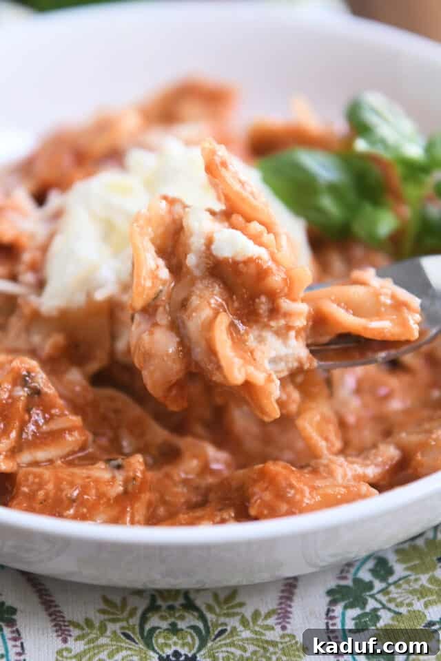 Effortless One-Pot Chicken Lasagna 7 A fork scooping a bite of one-pot chicken lasagna, showing the cheesy, saucy texture of the pasta and chicken.