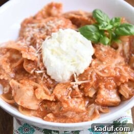 serving of chicken lasagna in white bowl with spoonful of ricotta and fresh basil leaves