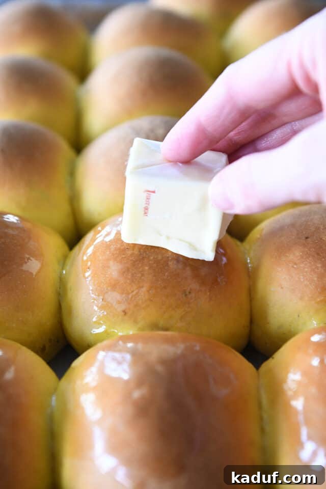 Aromatic Pumpkin Rosemary Rolls 6 A hand gently rubbing a cube of butter over the warm, fluffy surface of freshly baked pumpkin dinner rolls.