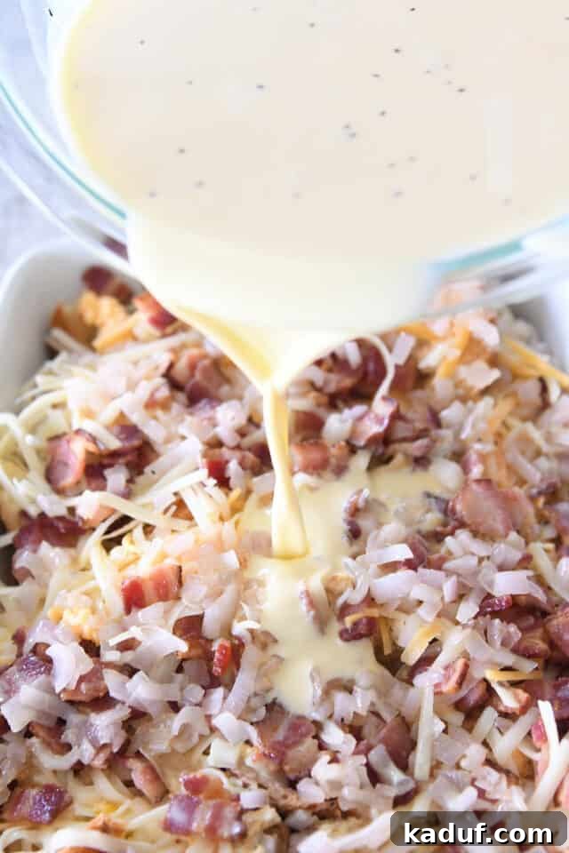 Overnight Cheesy Bacon Croissant Strata 5 Pouring rich egg and milk mixture over layered croissant, bacon, cheese, and onion ingredients in a white 9X13-inch pan.
