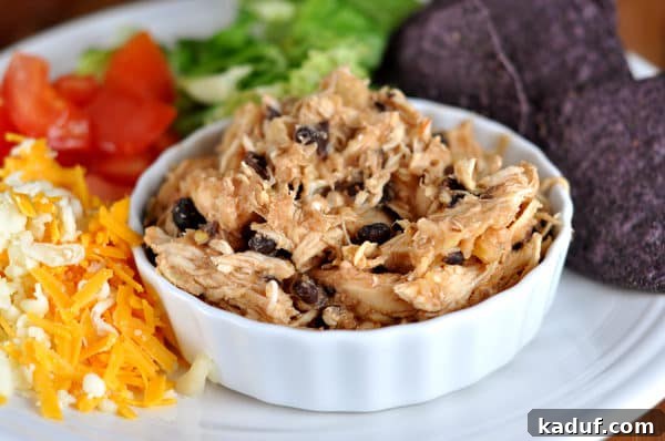 Easy Slow Cooker Pineapple Salsa Chicken 2 Small white ramekin filled with shredded pineapple salsa chicken and black beans, served on a larger plate with fresh toppings like shredded cheese, diced tomatoes, and crisp lettuce.
