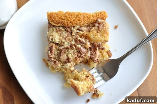 Buttery English Toffee Crunch Cake 3 Top view of a piece of Heath Bar cake on a white plate, with a fork taking a bite, highlighting the rich chocolate and toffee topping.