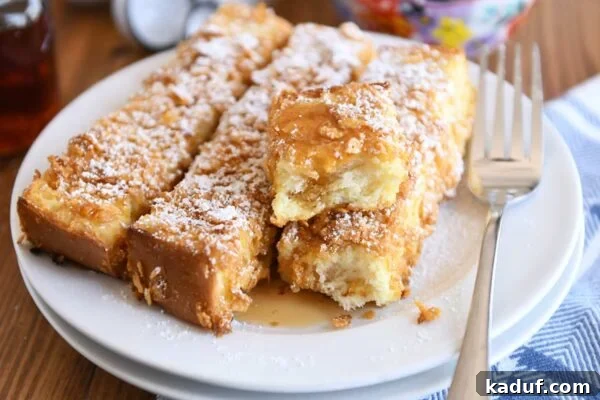 Crunchy baked French toast sticks on a white plate, generously dusted with powdered sugar and drizzled with maple syrup.