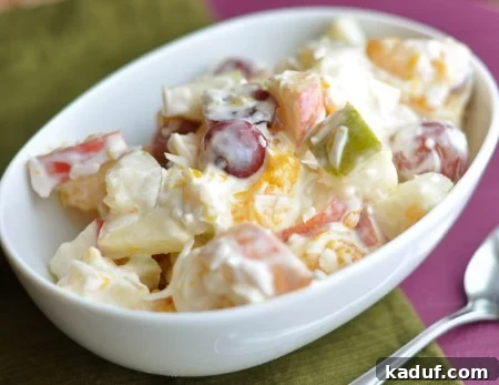 Velvety Fruit Ambrosia 3 White oval dish showcasing the glistening Creamy 5-Cup Fruit Salad, highlighting the rich coating and fresh fruit chunks from a slightly elevated angle.