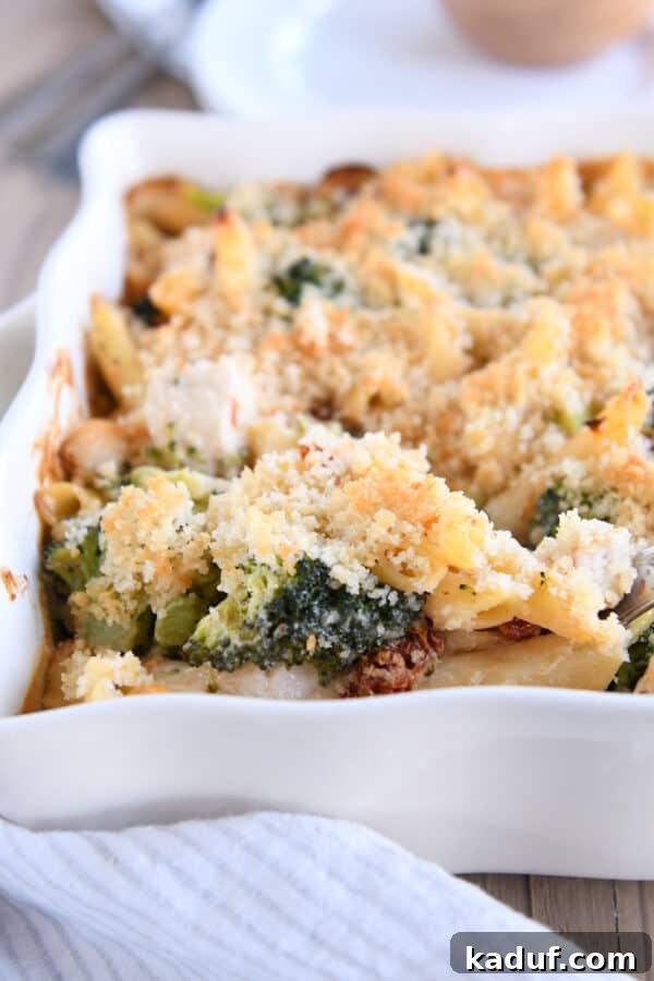 Smoky Mozzarella Chicken and Broccoli Penne Bake 7 A serving spoon lifting a generous scoop of baked penne, chicken, broccoli, and melted cheese from a white baking dish, showcasing the creamy interior and crispy topping.