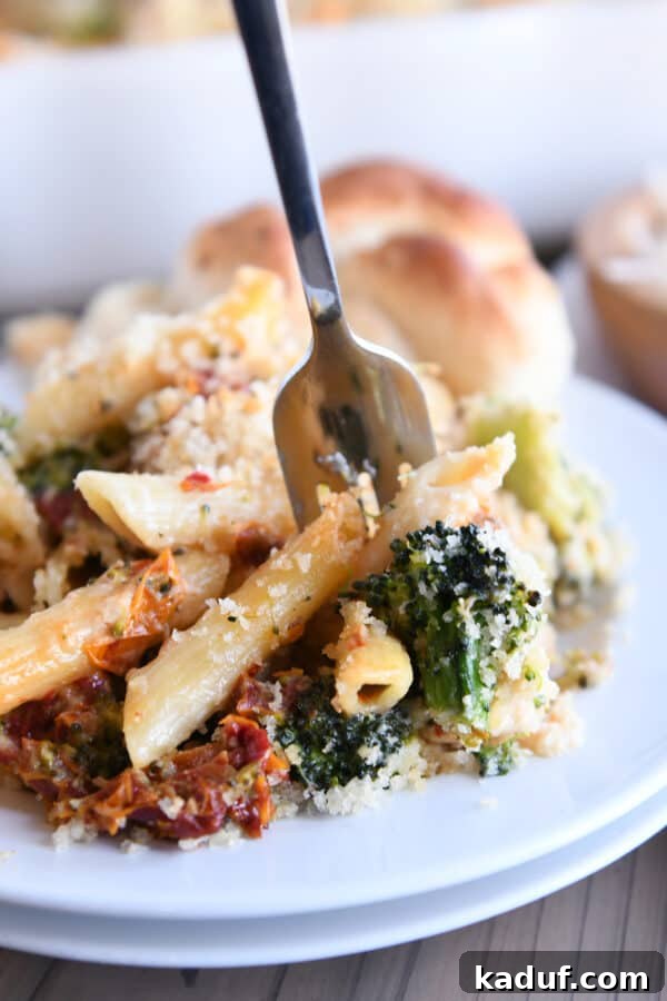 Smoky Mozzarella Chicken and Broccoli Penne Bake 8 A fork taking a bite of the baked penne, showing the creamy texture with chicken, broccoli, and sun-dried tomatoes.