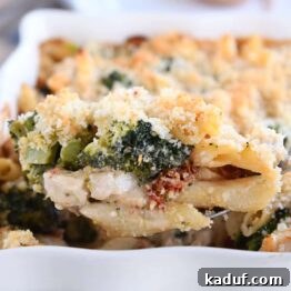 serving spoon taking scoop of baked penne out of white dish
