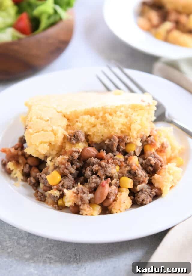 Ranch-Style Beef and Bean Cornbread Bake 2 Hearty cornbread topped beef, bean, and corn casserole on a white plate with a fork, ready to be enjoyed.