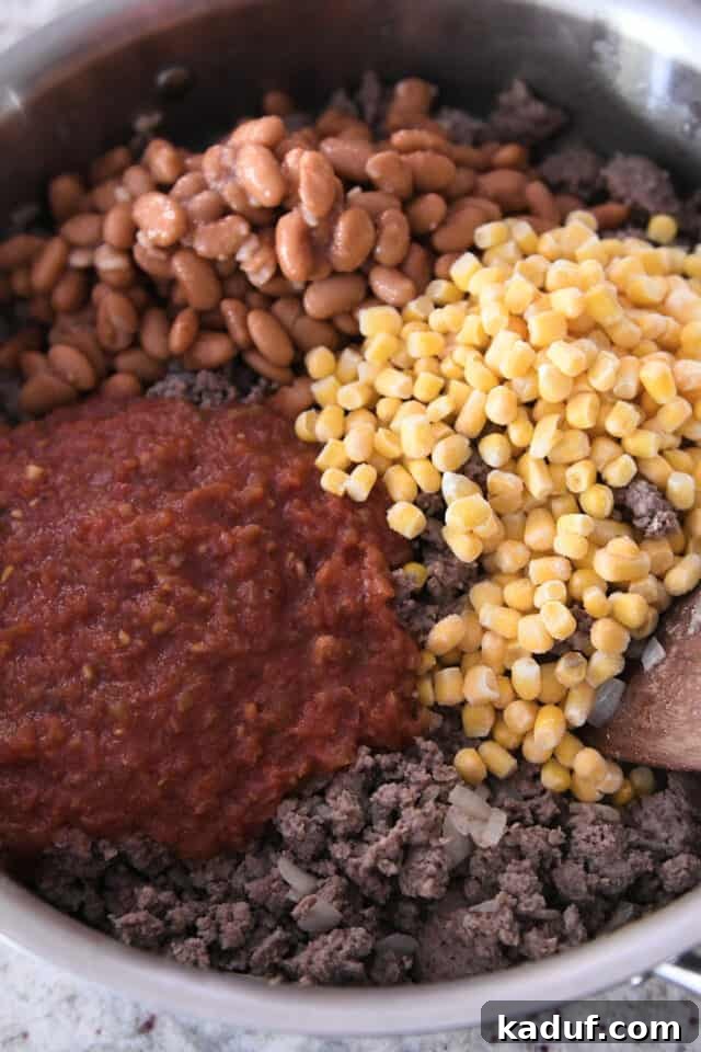 Ranch-Style Beef and Bean Cornbread Bake 3 Sautéed ground beef and onion mixed with vibrant salsa, pinto beans, and corn kernels in a stainless steel pan, forming the hearty base for the casserole.