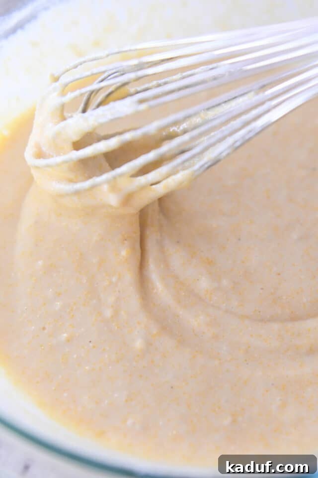 Ranch-Style Beef and Bean Cornbread Bake 4 A whisk gently stirring smooth, golden cornbread batter in a clear glass bowl, illustrating the quick and easy preparation of the topping.