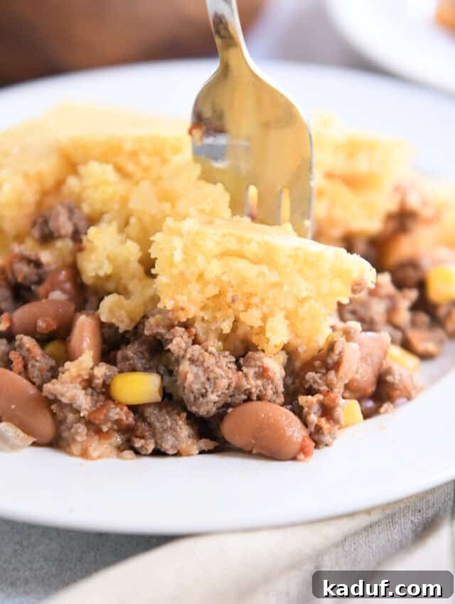 Ranch-Style Beef and Bean Cornbread Bake 7 A fork taking a delicious bite of the Cowboy Dinner Casserole, highlighting the tender cornbread, melted cheese, and hearty beef and bean filling.