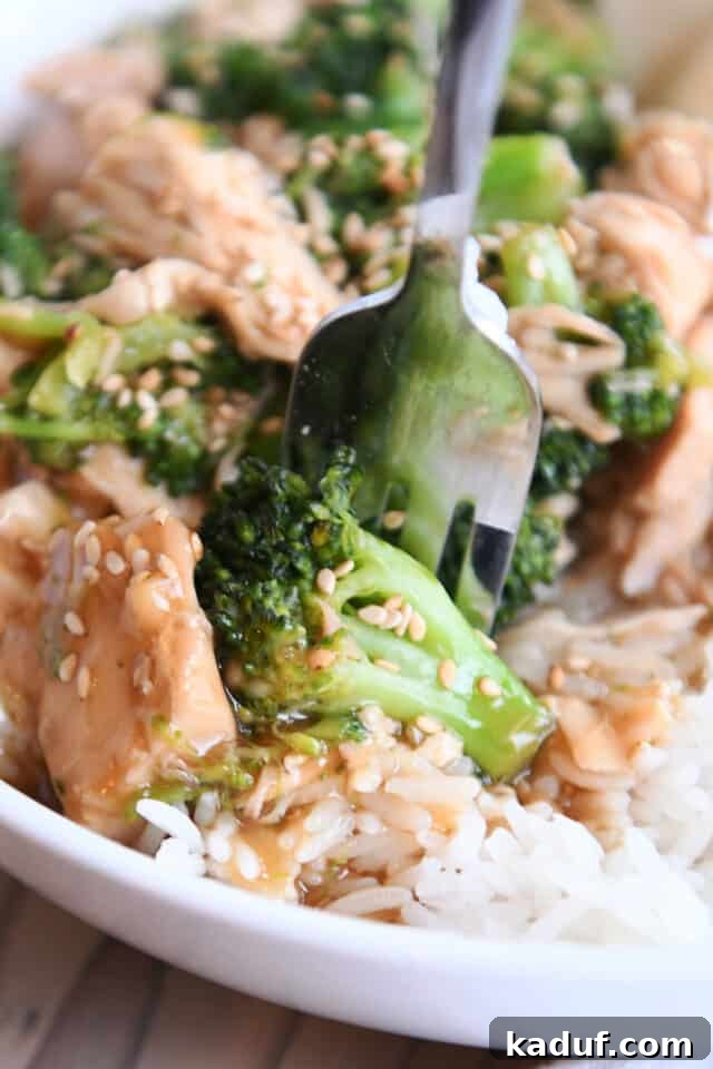 Effortless Chinese Chicken Broccoli Stir-Fry 4 White bowl with rice, broccoli, chicken, sesame seeds and fork, ready to eat.