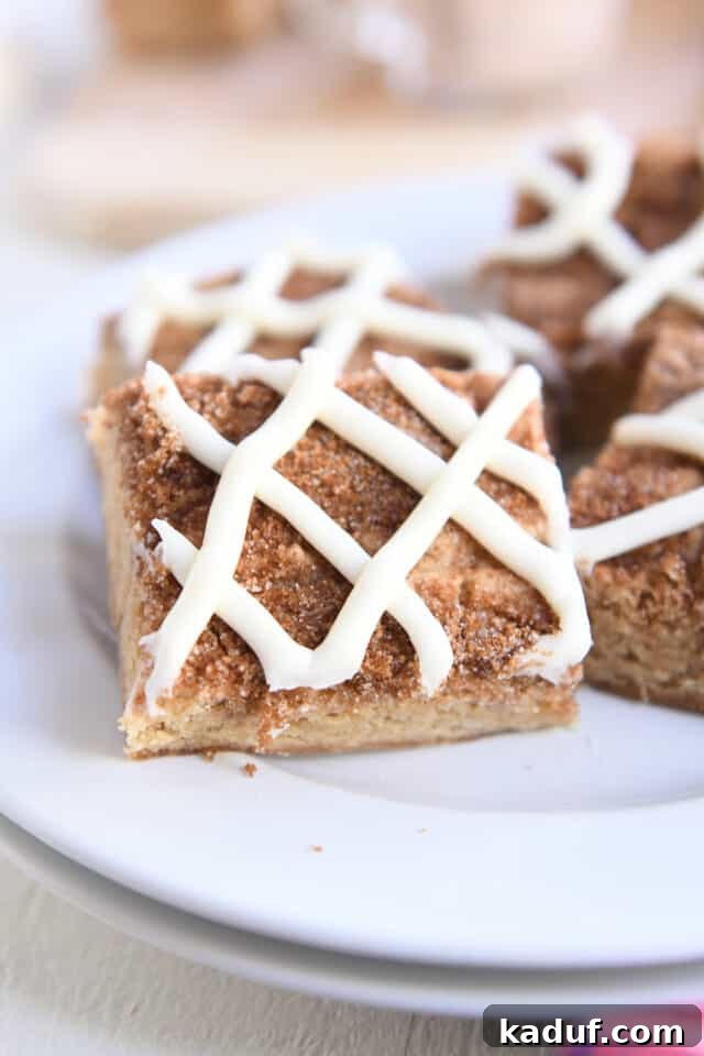 Cinnamon Roll Blondie Bars 6 Cinnamon roll blondie bar with cream cheese frosting swirl on white plate.