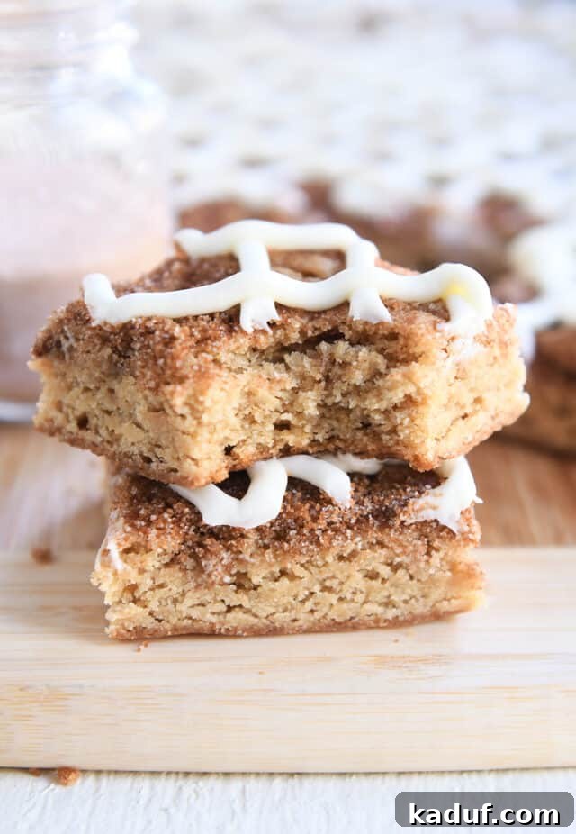 Cinnamon Roll Blondie Bars 7 Two cinnamon roll blondie bars stacked on each other on wood cutting board.