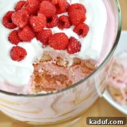 A vibrant Berrymisu Trifle topped with whipped cream and fresh raspberries, ready to be enjoyed.