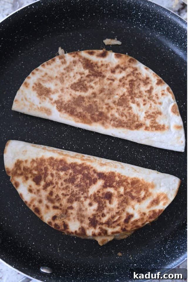 Irresistible Chicken Quesadillas 6 Two perfectly folded chicken quesadillas sizzling and browning in a hot skillet, showcasing their delicious golden crust.