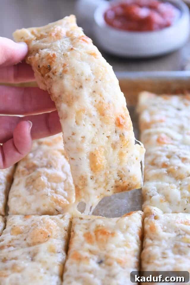Golden Cheesy Breadsticks 2 Holding one cheesy breadstick, golden brown with melted cheese.