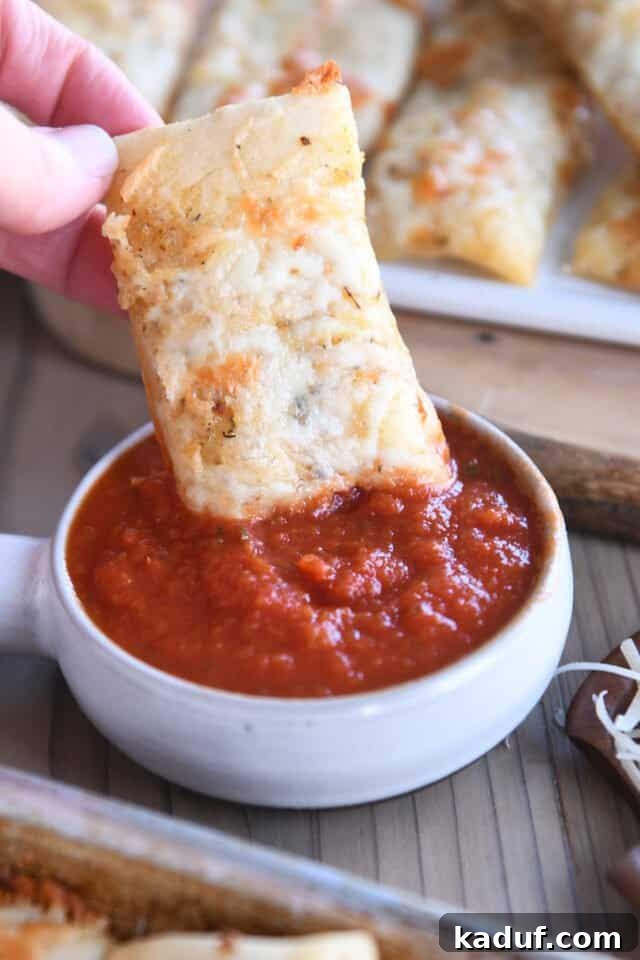 Golden Cheesy Breadsticks 7 A cheesy breadstick being dipped into a rich red marinara sauce.